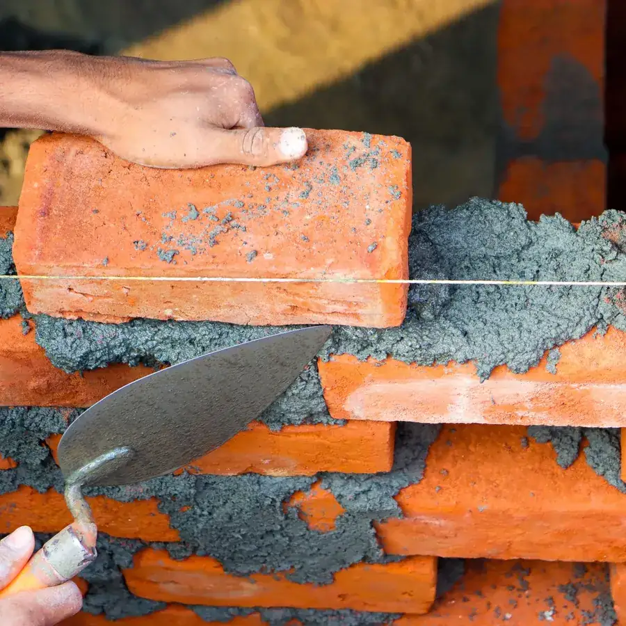 Hands laying red bricks with mortar